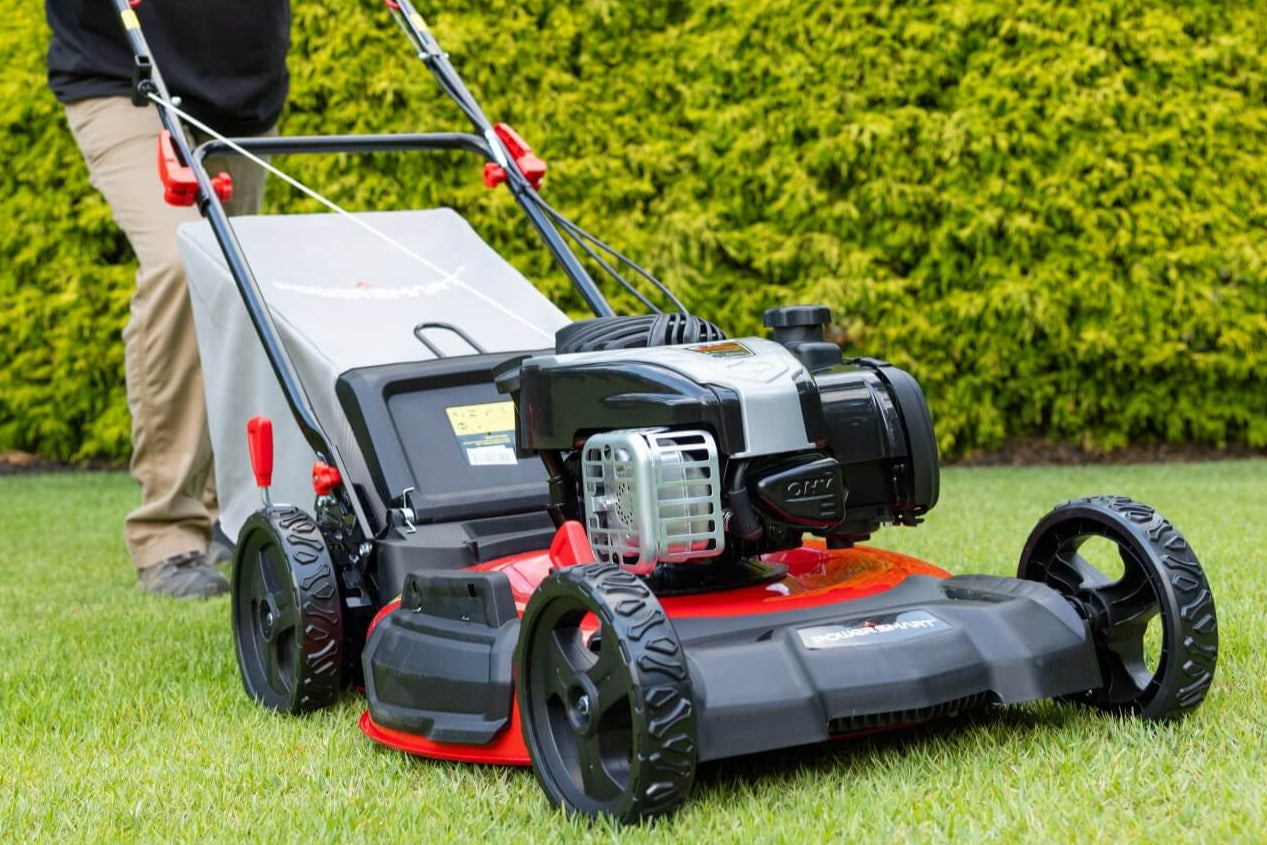 Person using a lawn mower on a grassy area with a hedge in the background